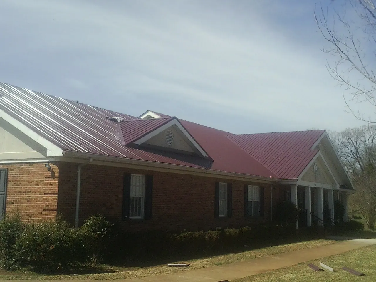 Red metal roof with gabled entries on a long brick building, from a Hail Damage Roof Repair job in Allison Park