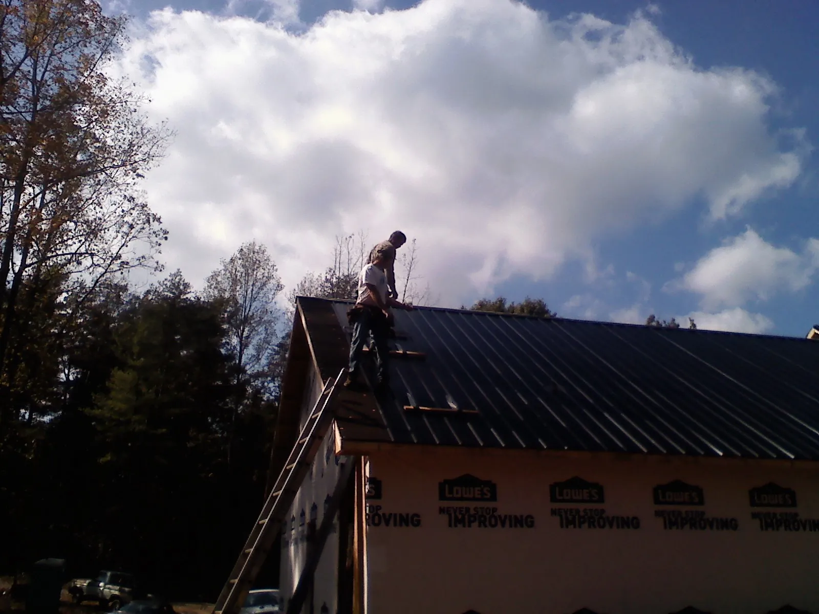 Roofer fastening dark metal panels high against a cloudy sky, from a Roof Inspection job in Allison Park