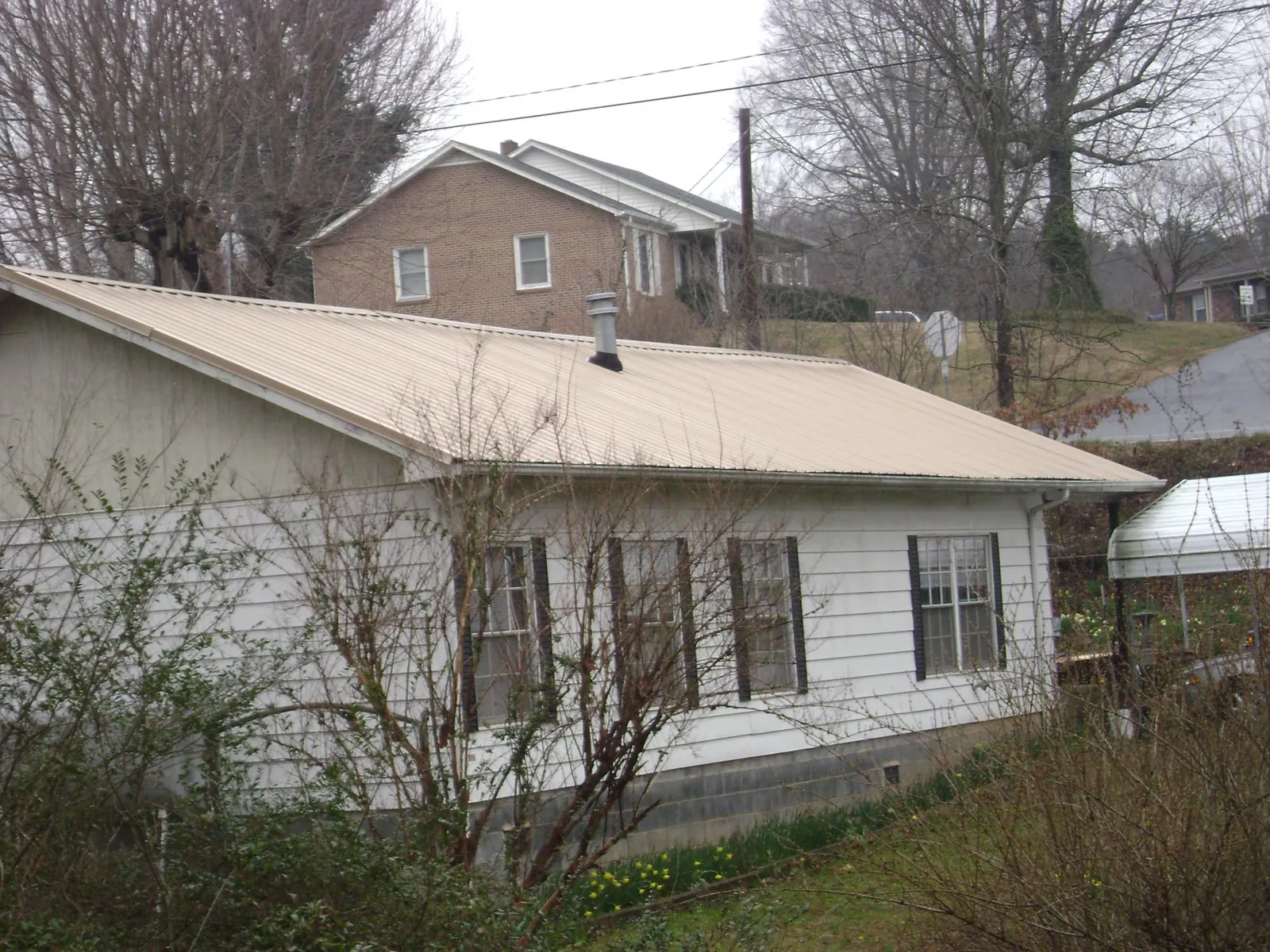 Tan metal roof on a white sided house set into a hillside — Commercial Roofing by Roofing Brothers in Allison Park